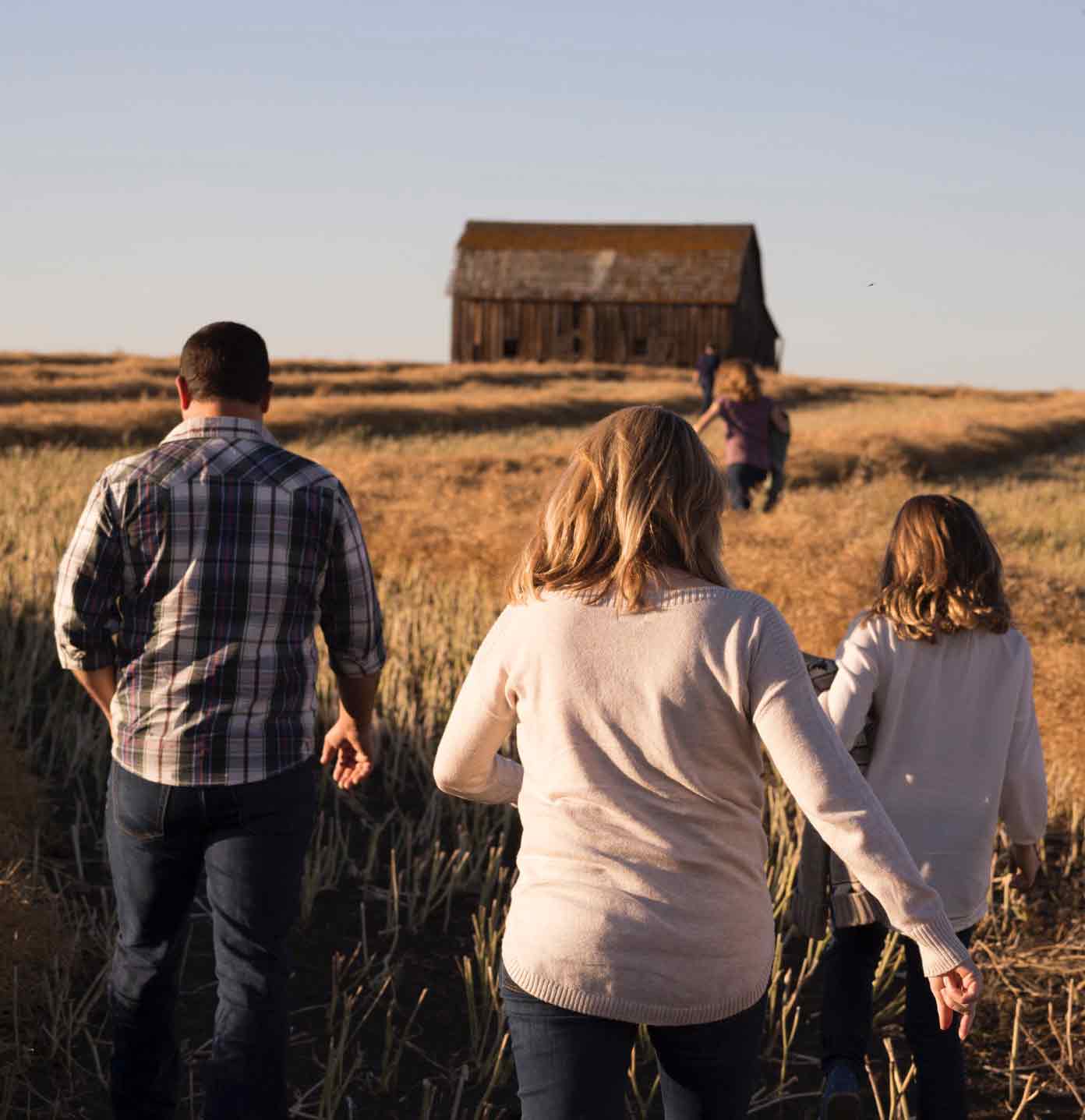 Famille courant dans les champs avec maison en arrière plan conseillée par un intermédiaire en assurances
